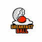 The Breakfast Ball (Sunnyside Up) Ball Marker by Logie Joe's Golf features a cracked golf ball with an orange yolk and BREAKFAST BALL in bold yellow-orange letters, perfect for quirky golf accessory fans.