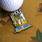 A close-up of the Ace Maker Ball Marker by Ballmarkers.com, a vibrant enamel pin shaped like a yellow excavator with "HOLE" in bold white letters, posed next to a golf ball on a textured brown surface to celebrate excavator golf.