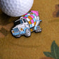 The Disco Mixer Ball Marker by Ballmarkers.com, shaped like a vibrant cement truck with a patchwork drum, rests beside a textured white golf ball on a fast greens-inspired patterned brown surface.