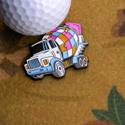 The Disco Mixer Ball Marker by Ballmarkers.com, shaped like a vibrant cement truck with a patchwork drum, rests beside a textured white golf ball on a fast greens-inspired patterned brown surface.