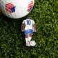 The Iconic #10 Ball Marker by Ballmarkers.com features a soccer player in a white #10 jersey on green grass and doubles as a unique golf ball marker with red, white, and blue shield patterns.