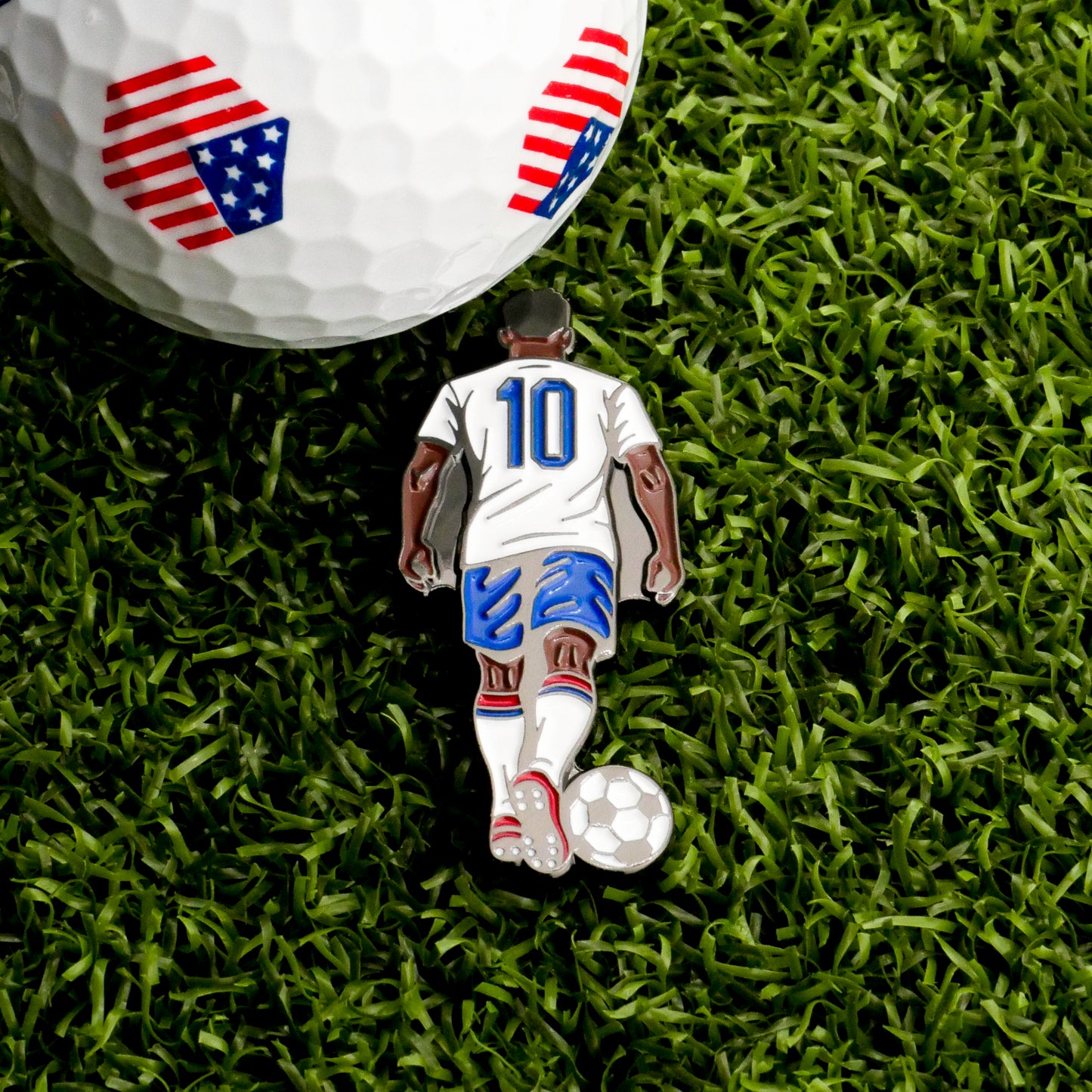 The Iconic #10 Ball Marker by Ballmarkers.com features a soccer player in a white #10 jersey on green grass and doubles as a unique golf ball marker with red, white, and blue shield patterns.