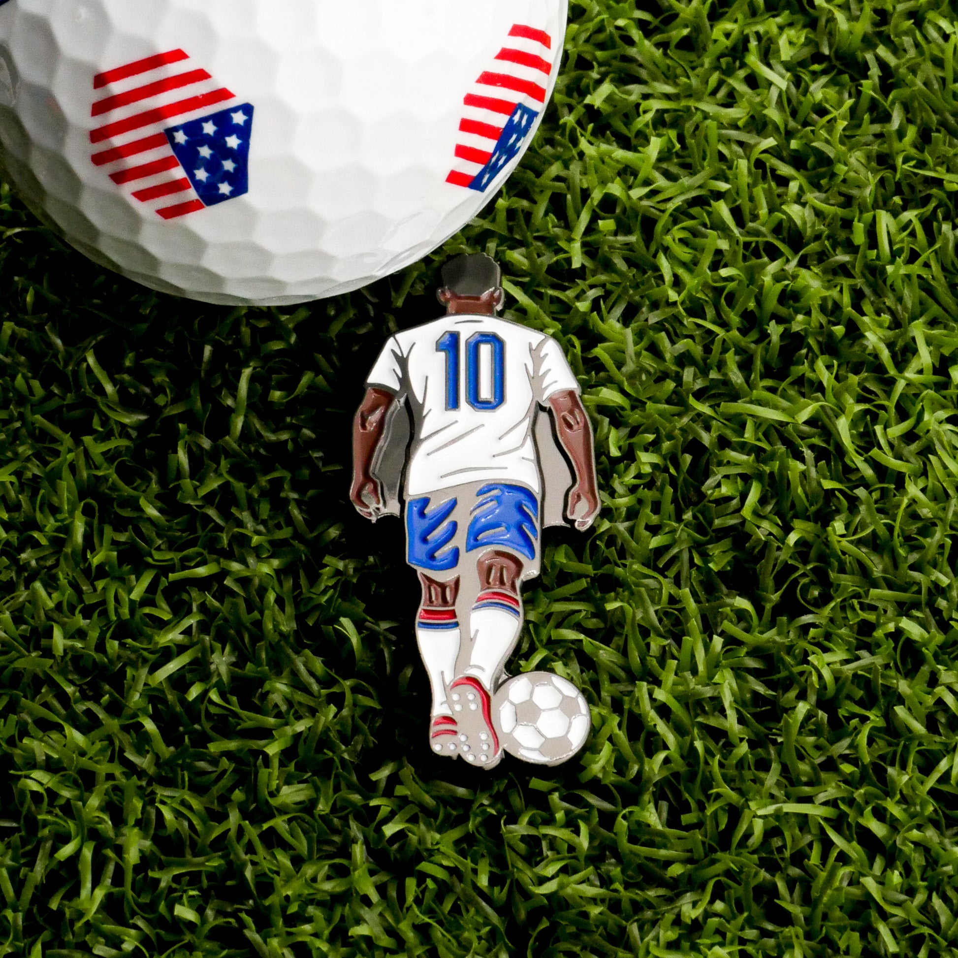 The Iconic #10 Ball Marker by Ballmarkers.com features a soccer player in a white #10 jersey on green grass and doubles as a unique golf ball marker with red, white, and blue shield patterns.