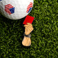 A close-up of an American flag golf ball with the Red Card Ball Marker by Ballmarkers.com, shaped like a referee's hand, displayed on green artificial turf.