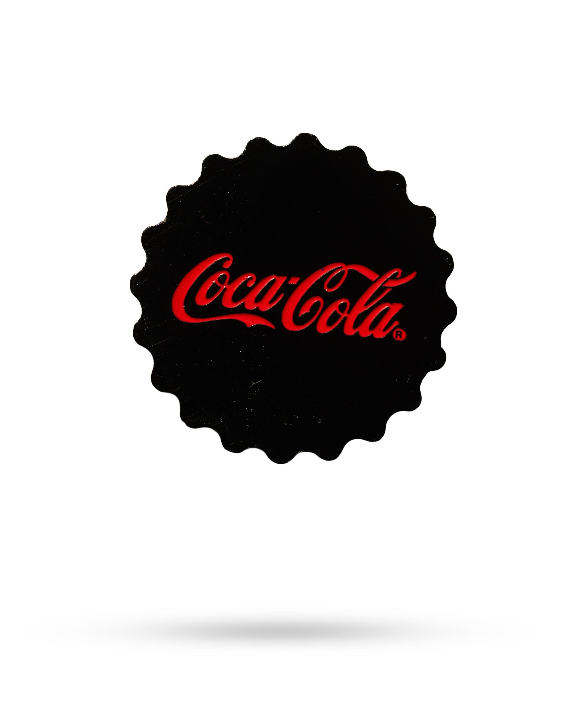 The Pins and Aces Coca-Cola Bottle Cap Ball Marker is a black, round magnetic hat clip featuring the red Coca-Cola logo in cursive at the center on a white background with a subtle shadow below.