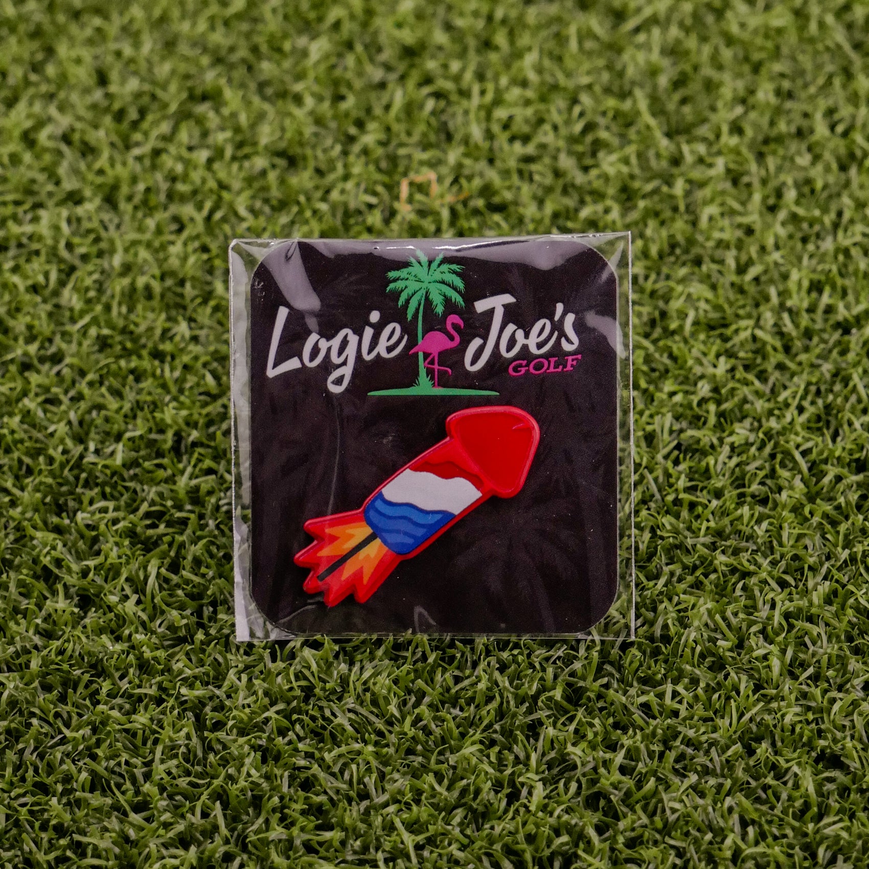 The Cock Rocket by Logie Joe's Golf is a vibrant rocket-shaped divot tool in branded packaging on green artificial grass—a fun and playful accessory for your collection of novelty golf gear.
