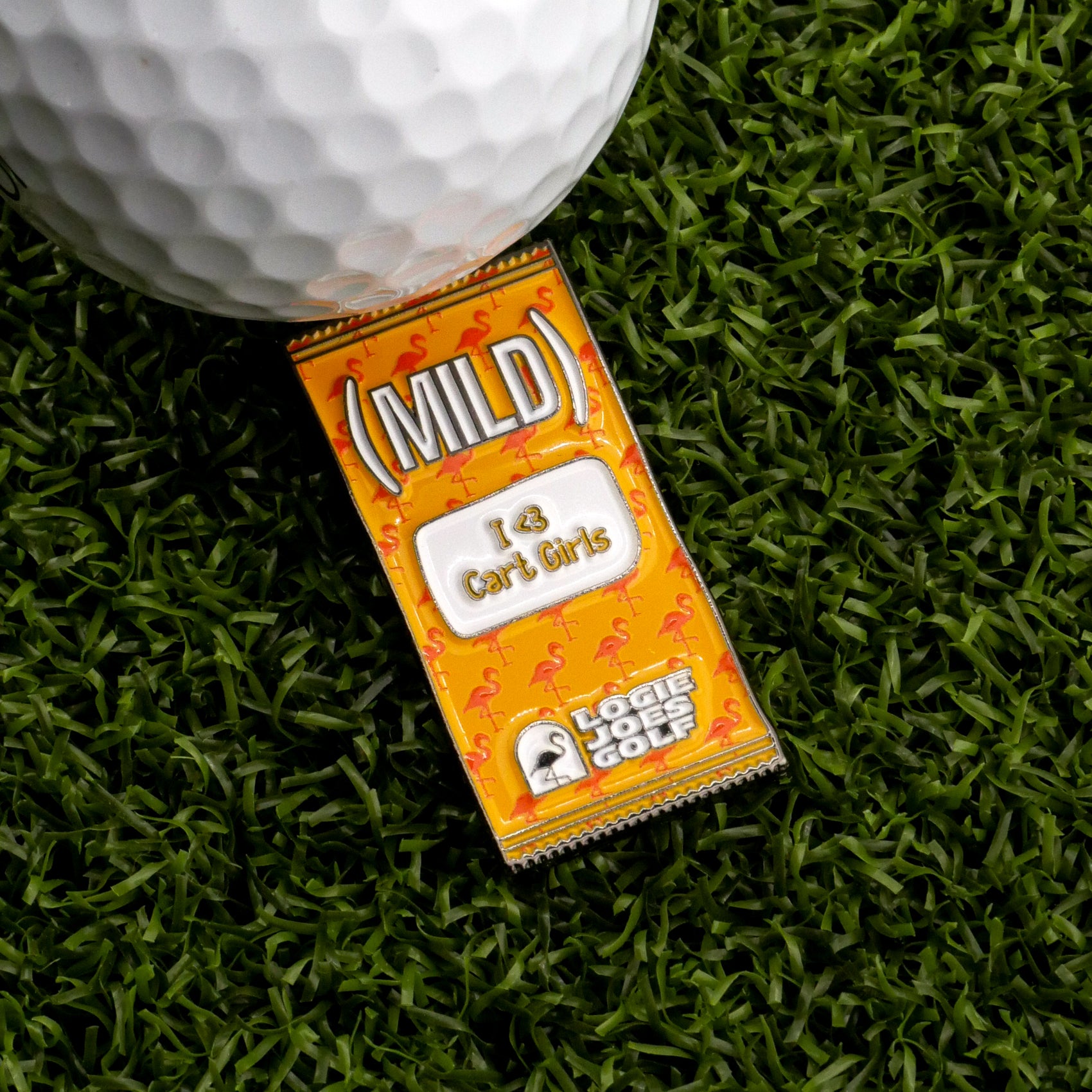 A golf ball and a Mild Taco Sauce Packet Ball Marker by Logie Joe's Golf rest on artificial grass—making a funny gift for golfers who love mild sauce.