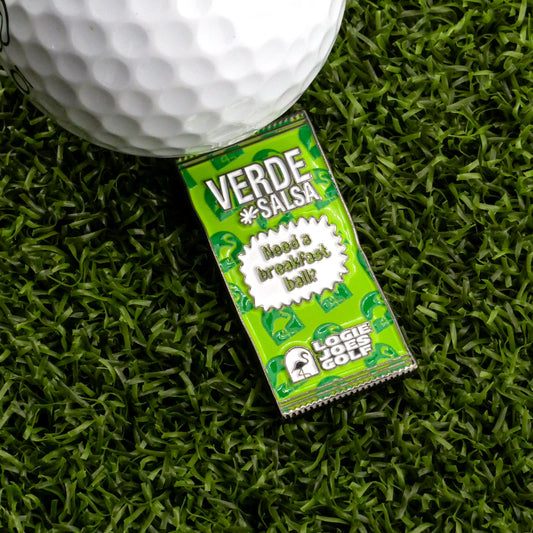 A Verde Salsa Taco Sauce Packet Ball Marker from Logie Joe's Golf, with golf-themed graphics, lies on artificial grass beside a white marker. The packet reads "Need a breakfast ball?" and displays the Logie Joe's Golf logo and a humorous message.