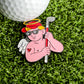 A golf ball rests on grass beside the Ballmarkers.com Cupid of Golf Ball Marker—a fun pin with a cartoon angel in sunglasses and a red cap holding a club, perfect as a golfer gift or for Valentine's Day.