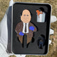 A gloved hand holds Pin Creatures’ Chili Cook Off Divot Tool set—a metal box with golf accessories in foam slots, featuring a cartoon bald man in a suit with blue gloves, a spilled chili pot, a black object, and a ball marker.
