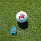 A golf ball with "YOU SUCK" in red on green grass sits beside Shank it Golf's Blobert Ball Marker—a colorful, premium metal magnetic marker featuring a blue melting cartoon face in a gray cap.