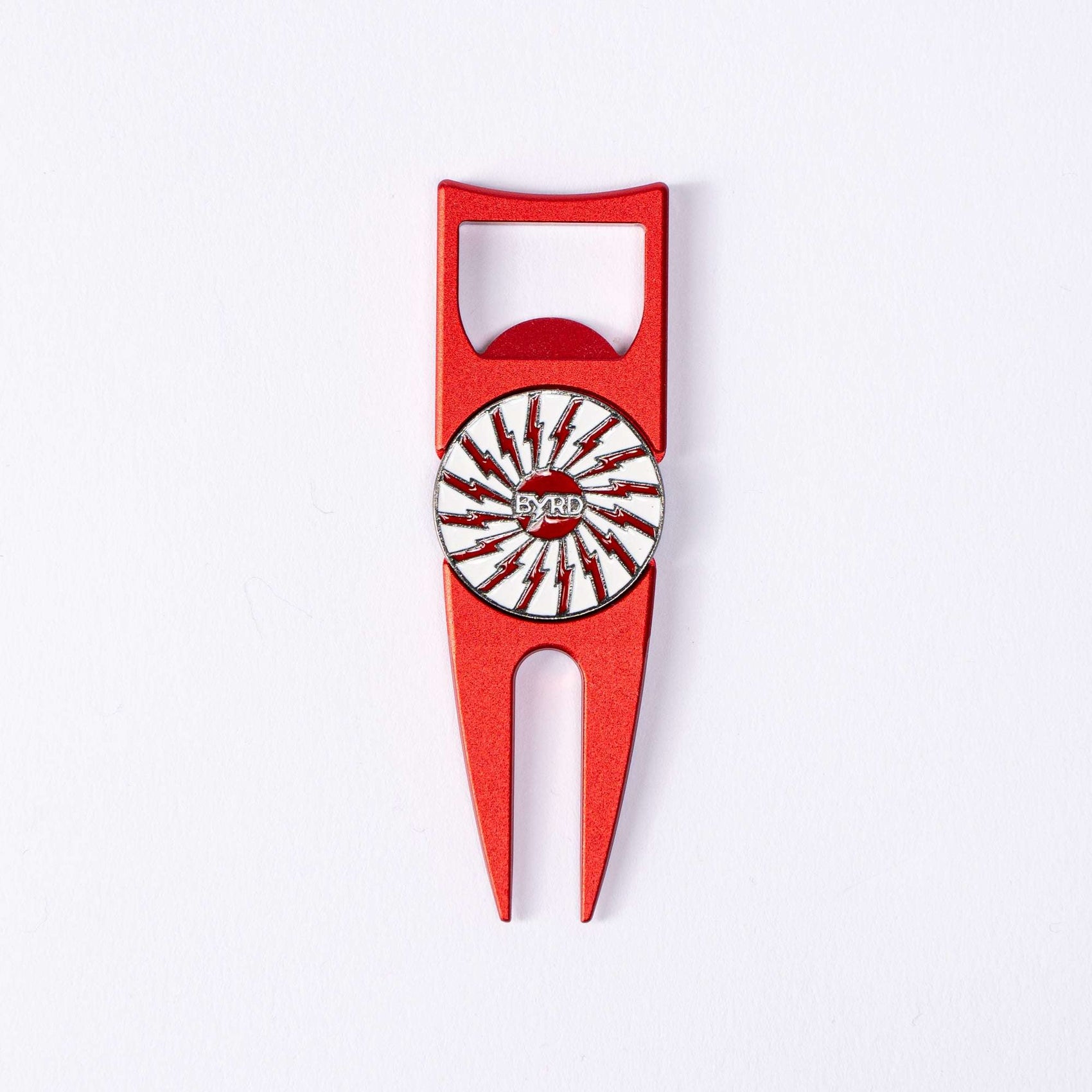 The BYRD DIVOT TOOL - 4 in 1 by The Byrd, LLC is a red metal golf tool with a circular design and black/red lightning bolts in the center, plus a built-in ball marker holder, shown on a white background.