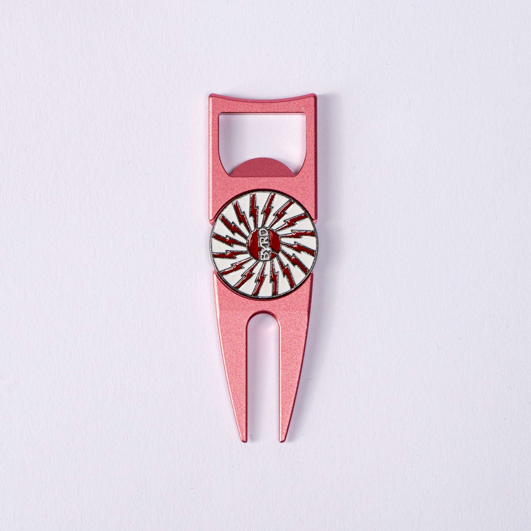 The Byrd, LLC BYRD DIVOT TOOL - 4 in 1 is a pink metal golf divot tool and ball marker holder with a white circular emblem featuring red lightning bolts and "REVOLT" in the center, shown on a plain white background.