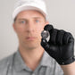 A person in a white cap and gray shirt, wearing a black glove, holds Doubloon’s The Omen Classic Antique, Diamond & Silver Edition golf ball marker toward the camera; their face is out of focus in the background.
