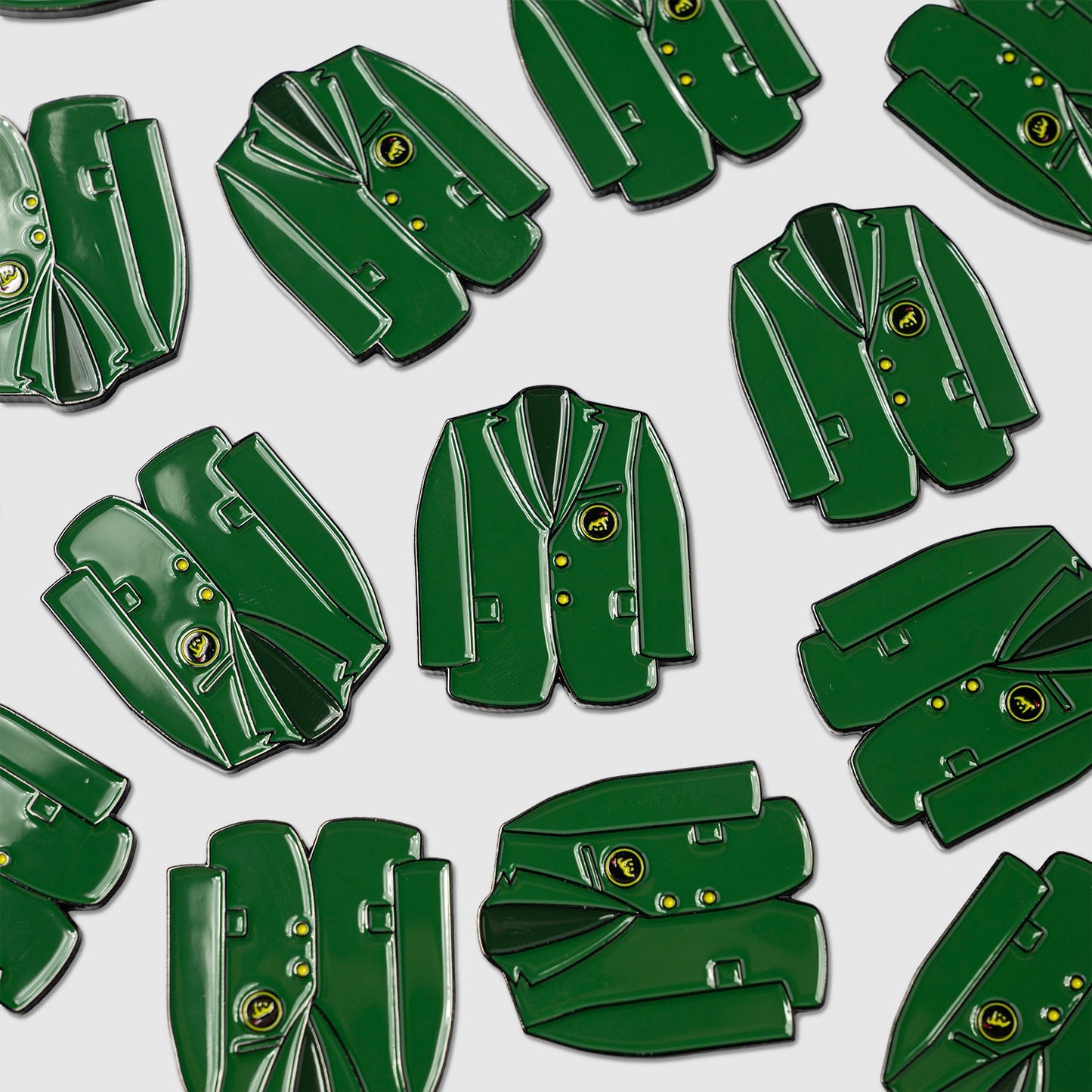 Several Guerrilla Golf Green Coat Ball Marker pins are scattered across a light gray background, each featuring gold-tone buttons and a distinctive yellow emblem.