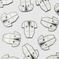 Pattern of white Guerrilla Golf Caddy Bib Ball Markers shaped like lab coats, with green patches and pocket details—each designed as a novelty marker—arranged evenly on a light gray background.
