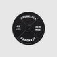 A black 45lb Plate Ball Marker by Guerrilla Golf, featuring "GUERRILLA STANDARD" along with weight markings of 45 LBS and 20.4 KGS in crisp white text against a light gray backdrop—its robust design evokes the industrial strength of a manhole cover.