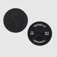 Two black Guerrilla Golf 45lb Plate Ball Markers on a light gray background; one marker displays the GUERRILLA STANDARD 45 LBS 20.4 KGS text, while the other is turned over, its blank side resembling a manhole cover.