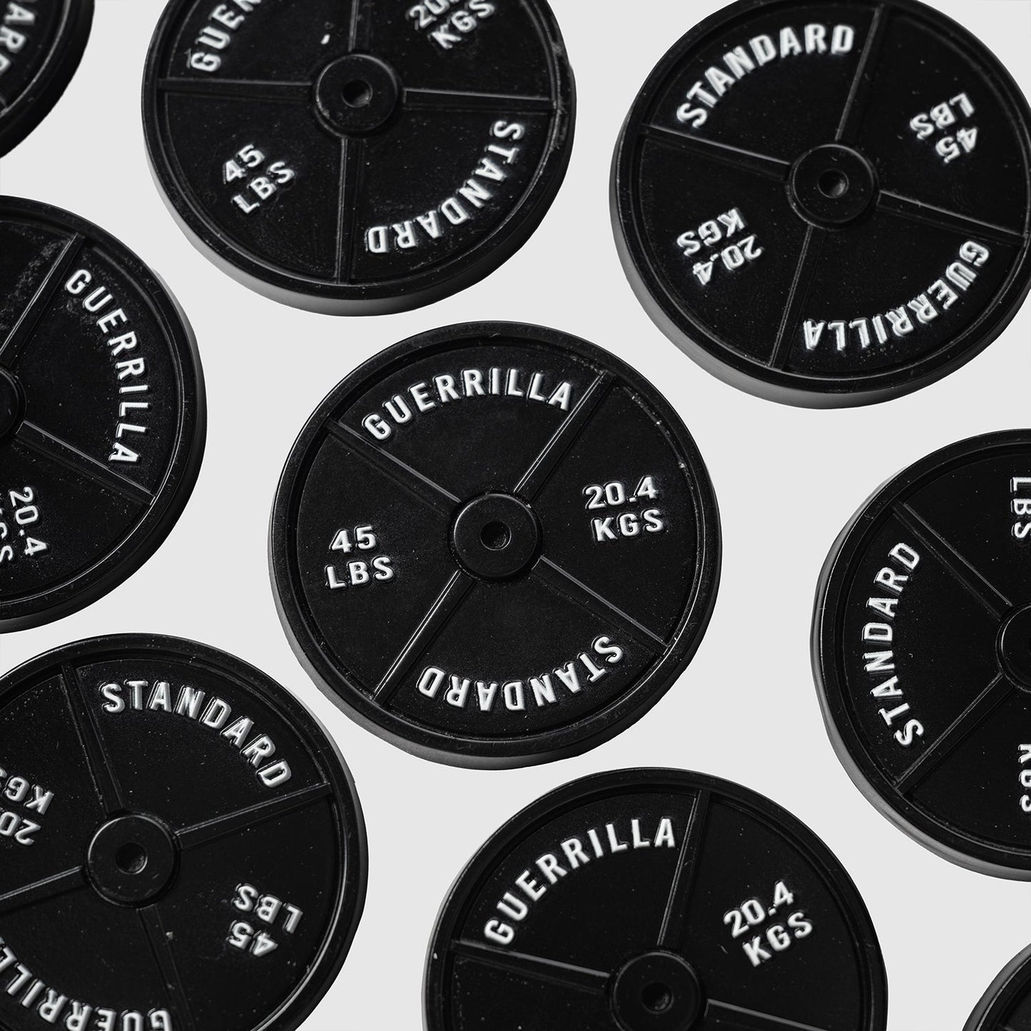 Several black 45lb Plate Ball Markers from Guerrilla Golf, each labeled GUERRILLA STANDARD 45 LBS 20.4 KGS, are arranged on a white background and viewed from above, resembling the classic 45 plates found in gyms.