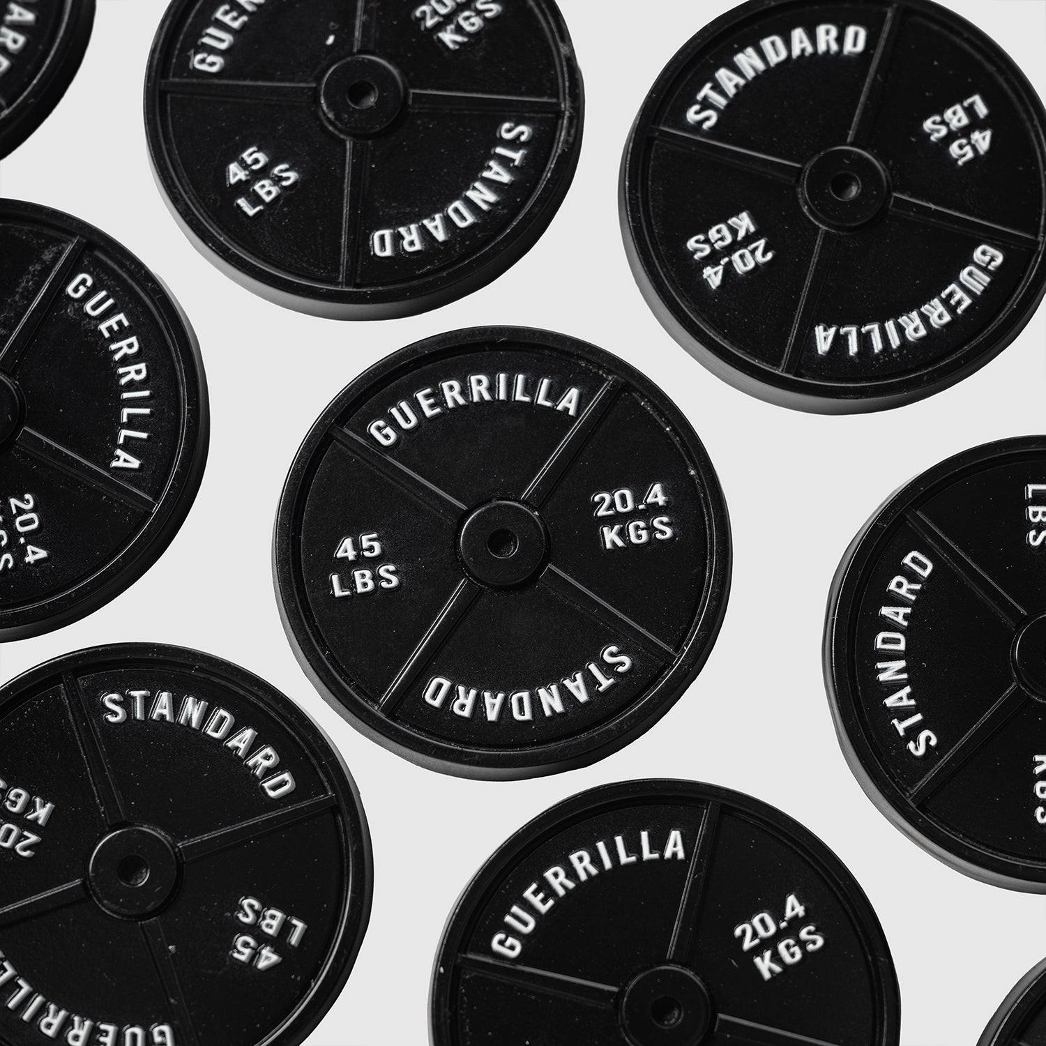 Several black 45lb Plate Ball Markers from Guerrilla Golf, each labeled GUERRILLA STANDARD 45 LBS 20.4 KGS, are arranged on a white background and viewed from above, resembling the classic 45 plates found in gyms.