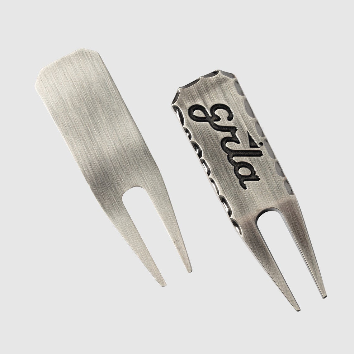 Two GRLA Raw Divot Tools by Guerrilla Golf, crafted from metal with a brushed finish—one featuring the smooth reverse and the other highlighting a textured face engraved with the bold black GRLA logo. This must-have accessory seamlessly blends durability and style for every golfer.