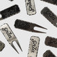 The Guerrilla Golf GRLA Raw Divot Tool, crafted from premium metal and engraved with the elegant GRLA logo, is artfully displayed on a light background. This standout accessory merges functional design with sophisticated style.