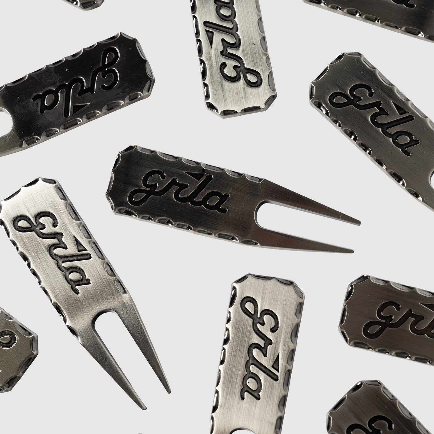 The Guerrilla Golf GRLA Raw Divot Tool, crafted from premium metal and engraved with the elegant GRLA logo, is artfully displayed on a light background. This standout accessory merges functional design with sophisticated style.
