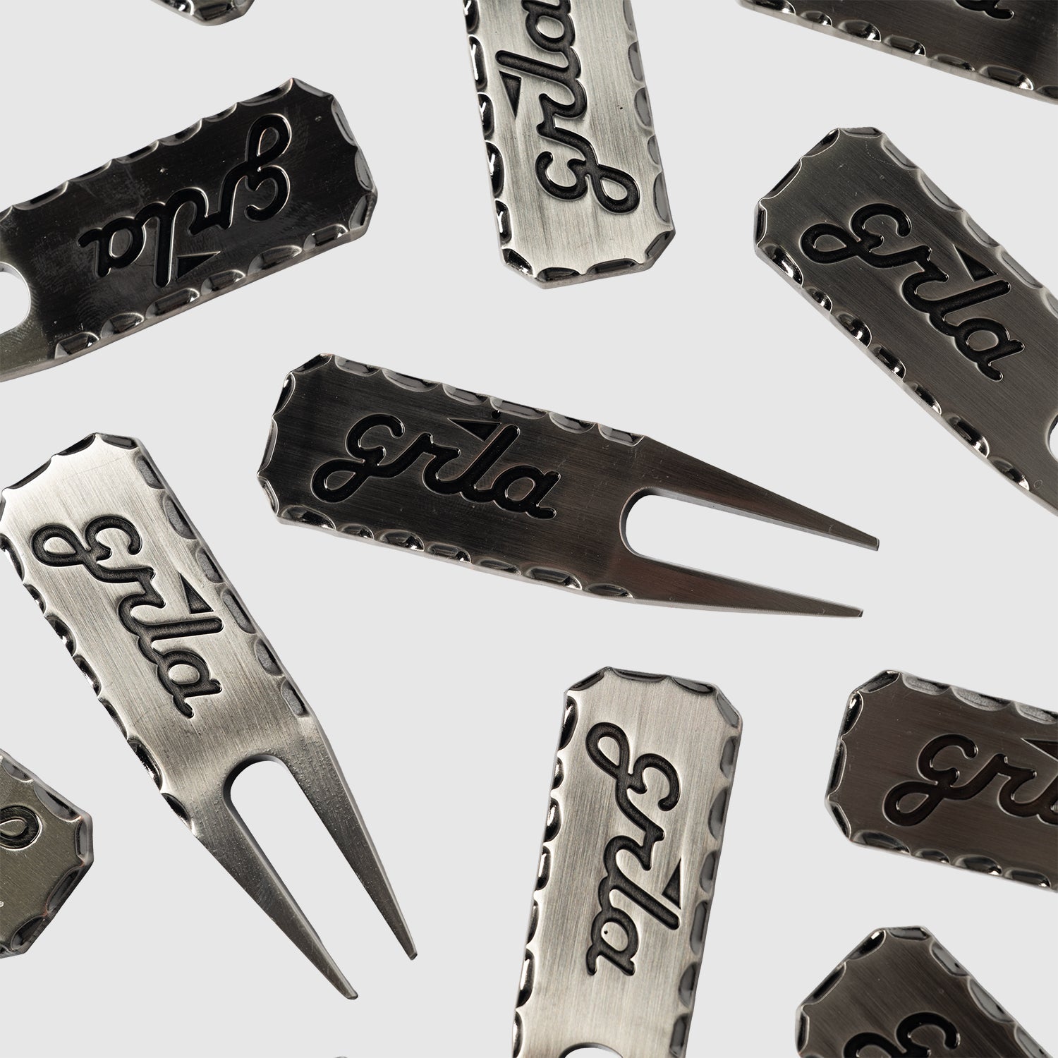 The Guerrilla Golf GRLA Raw Divot Tool, crafted from premium metal and engraved with the elegant GRLA logo, is artfully displayed on a light background. This standout accessory merges functional design with sophisticated style.