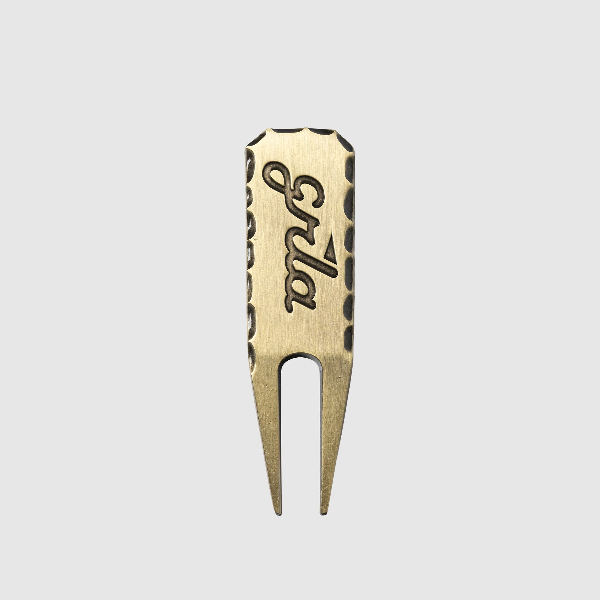 The Guerrilla Golf GRLA Raw Divot Tool, crafted from brass and engraved with "Spla," showcases textured edges and the official GRLA logo. Presented against a plain light gray background, this accessory embodies elegance for every golf enthusiast.