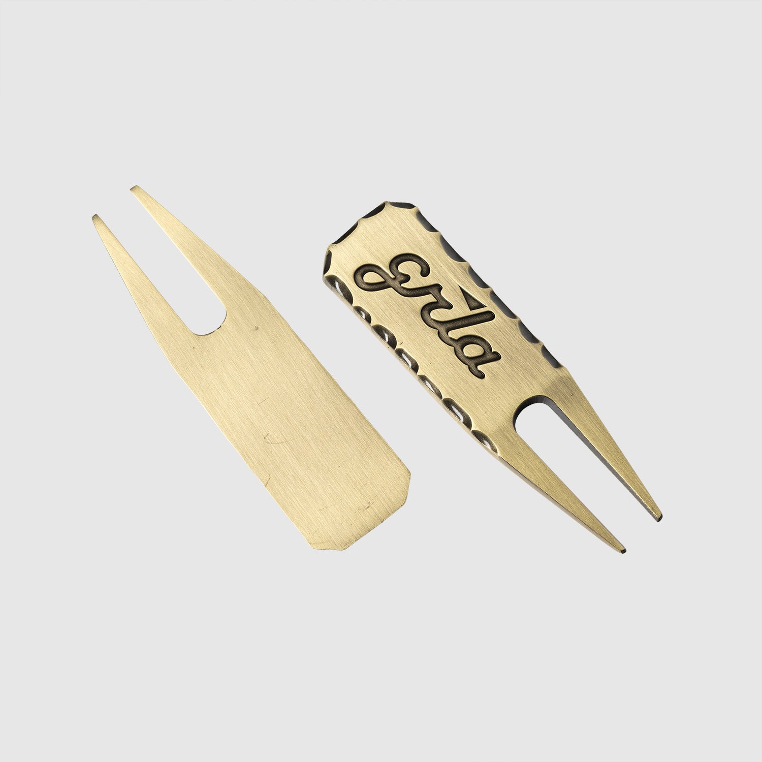 Two Guerrilla Golf GRLA Raw Divot Tools are shown on a plain background; one tool is unadorned, while the other—a stylish golf accessory—features an engraved "Erika" and a patterned edge displaying the GRLA logo.