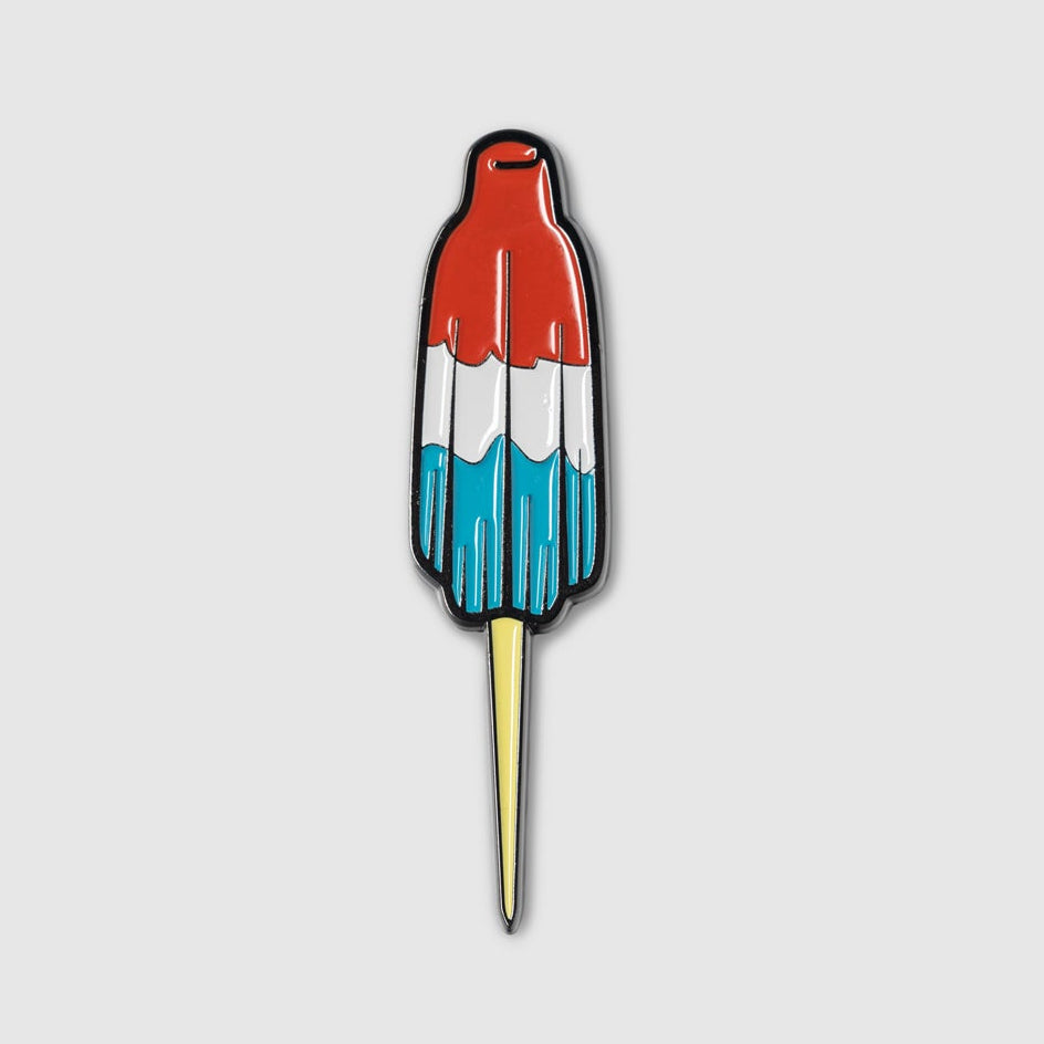 Add patriotic flair to your golf game with the Guerrilla Golf Rocket Pop Divot Tool, designed to look like a classic red, white, and blue rocket pop ice cream treat with a bright yellow stick—set against a plain light gray background.