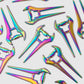 Several Guerrilla Golf E Sword Divot Tools are scattered on a white background, each featuring a metallic rainbow finish and an iridescent, angular design reminiscent of a sleek hair stick—an eye-catching golf accessory that makes its mark in one shot.