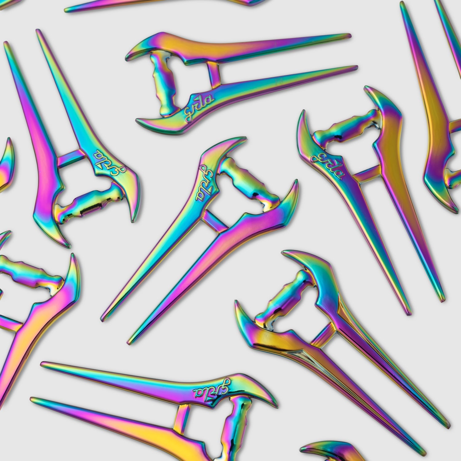 Several Guerrilla Golf E Sword Divot Tools are scattered on a white background, each featuring a metallic rainbow finish and an iridescent, angular design reminiscent of a sleek hair stick—an eye-catching golf accessory that makes its mark in one shot.