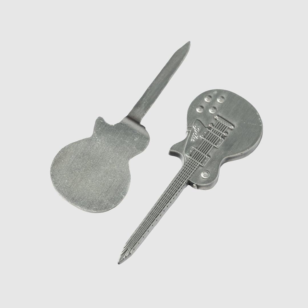 Two metal tools from Guerrilla Golf, shaped like electric guitars—one flat and one engraved with detailed guitar accents—are displayed on a simple grey background, highlighting the distinctive Guitar Divot Tool set.