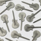 Several Guerrilla Golf Guitar Divot Tools, each crafted from metal and shaped like an electric guitar with embossed details such as strings, knobs, and pickups, are scattered on a white surface—making them the perfect accessory for golf enthusiasts who want to add a musical twist to their game.