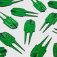 Several Guerrilla Golf Green Coat Divot Tools, each designed as a green jacket-shaped lapel pin with two long pins reminiscent of a classic golf divot tool, are arranged on a light gray background.