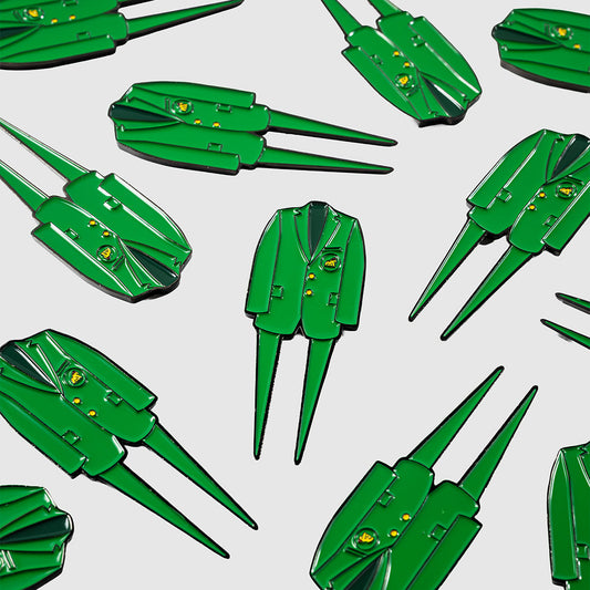 Several Guerrilla Golf Green Coat Divot Tools, each designed as a green jacket-shaped lapel pin with two long pins reminiscent of a classic golf divot tool, are arranged on a light gray background.
