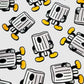 Fat Cap Ball Markers by Guerrilla Golf are illustrated in a repeating pattern on a white background, with each marker depicted as a cartoon character featuring arms, legs, and yellow shoes, enhanced with playful NY fat graffiti details for an added urban edge.