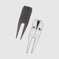Showcased here are two Guerrilla Golf Caddy divot tools—ideal golf gifts for any enthusiast. One features a textured, engraved finish with the Guerrilla Golf branding, while the other stands out as a unique divot repair tool styled like a white suit jacket with lapels and two green postage-stamp details. Both are displayed against a plain white background, making this stylish set an eye-catching addition to any golfer’s collection.