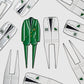 A green Caddy divot tool by Guerrilla Golf, shaped like a jacket and the perfect golf accessory or gift, is surrounded by white jacket-shaped Caddy divot tools adorned with golf-themed patches and numbers, all displayed on a white background.