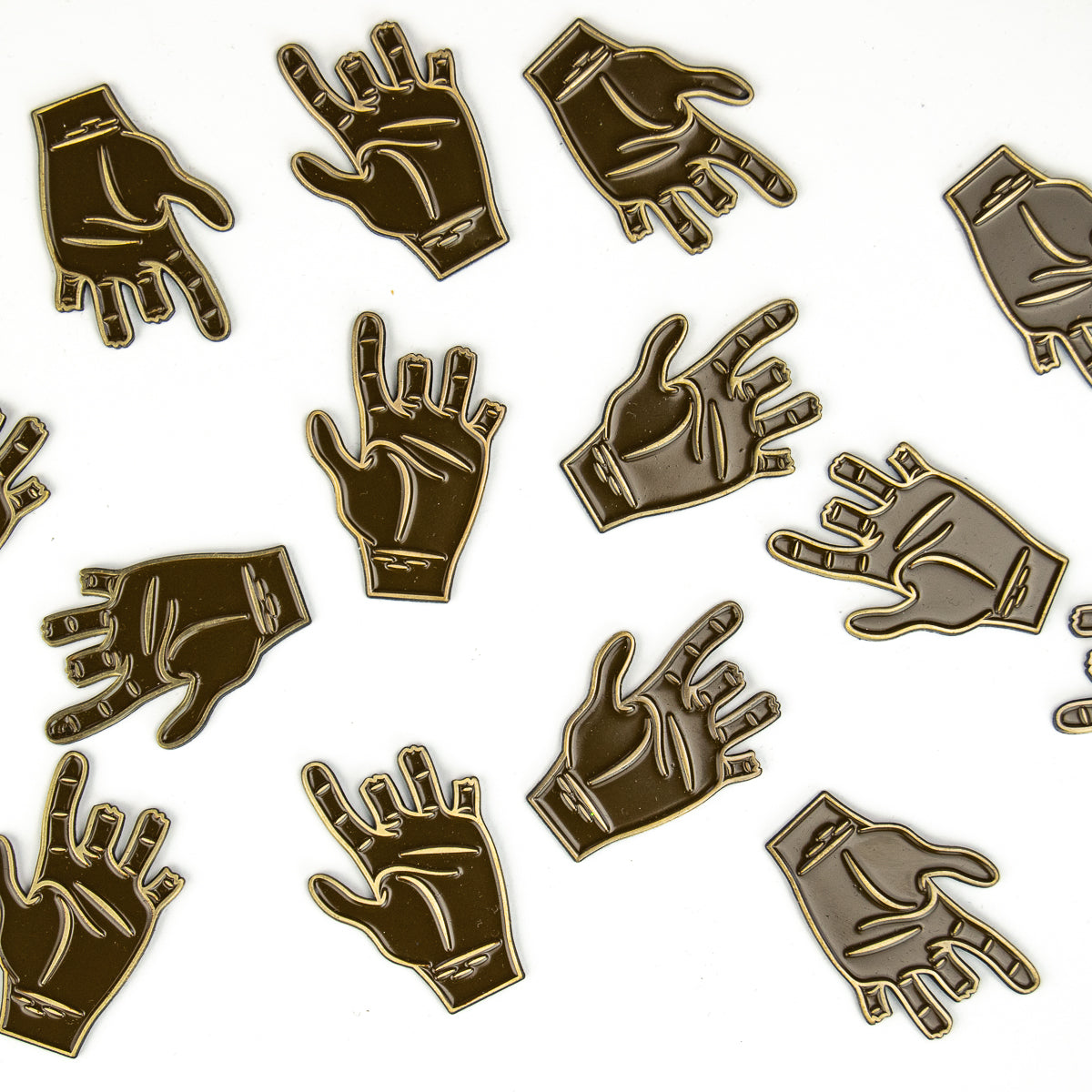 A collection of gold-colored metal pins shaped like hands with various gestures are arranged on a white surface, each outlined in black. These distinctive Chubbs Ball Markers by Guerrilla Golf serve as both stylish accessories and functional golf ball markers—perfect for honoring classic golf moments or referencing iconic characters. Each hand gesture brings unique personality and flair to your game.