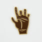 Introducing the Chubbs Ball Marker by Guerrilla Golf—a brown enamel pin featuring a hand making the ASL "I love you" sign, outlined in gold on a white background. This unique accessory makes an ideal golf ball marker or a thoughtful gift for any golfer.