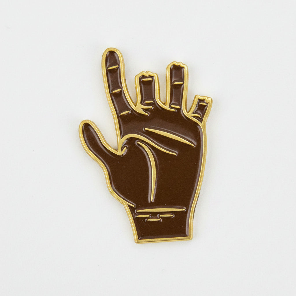 Introducing the Chubbs Ball Marker by Guerrilla Golf—a brown enamel pin featuring a hand making the ASL "I love you" sign, outlined in gold on a white background. This unique accessory makes an ideal golf ball marker or a thoughtful gift for any golfer.