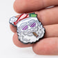 A hand holds Pins and Aces' "Santa the Degenerate Ball Marker," a fun enamel pin showing Santa with pink sunglasses, a cigar, and cash in his hat—an ideal magnetic golf marker or Christmas golf accessory for the festive season.