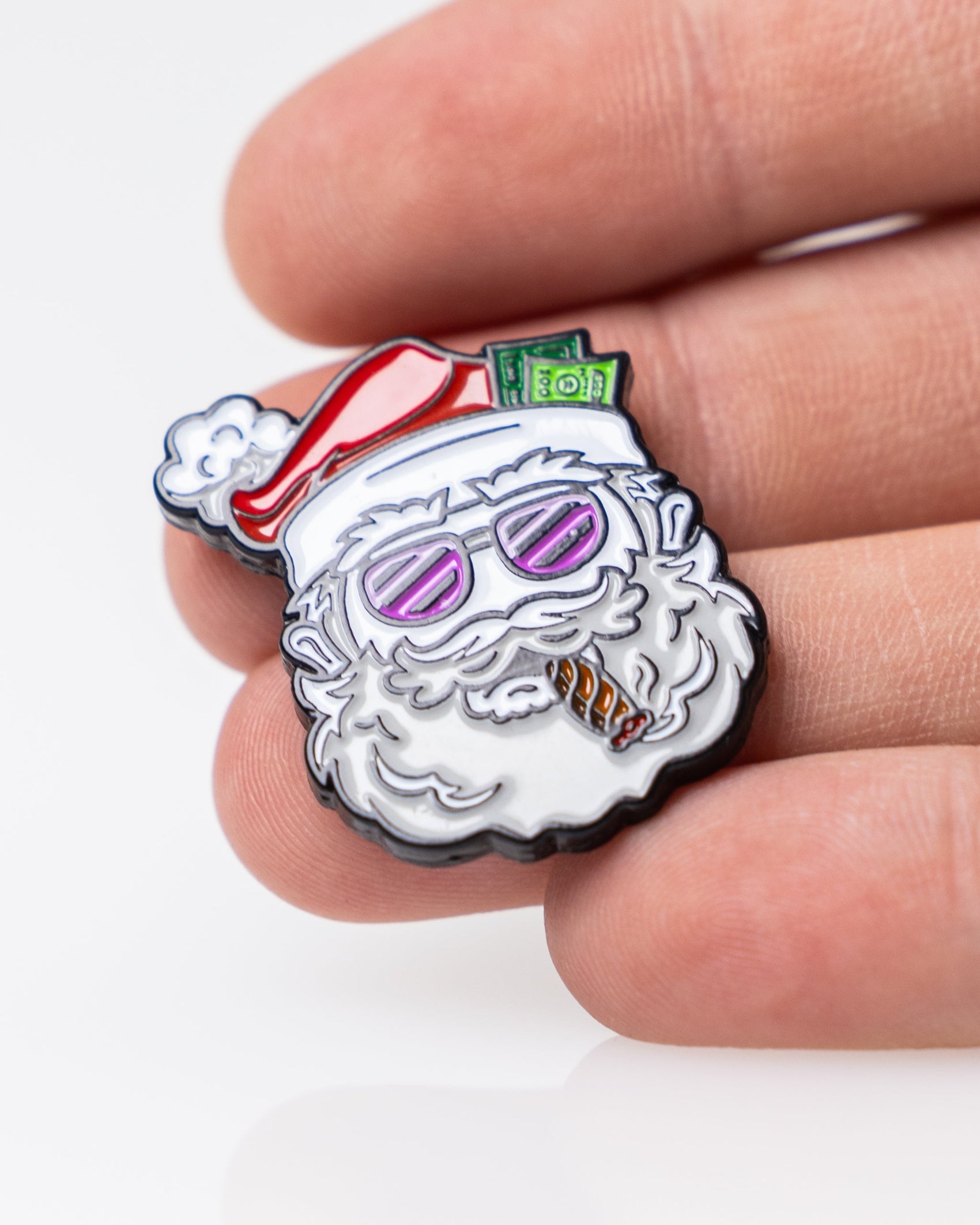 A hand holds Pins and Aces' "Santa the Degenerate Ball Marker," a fun enamel pin showing Santa with pink sunglasses, a cigar, and cash in his hat—an ideal magnetic golf marker or Christmas golf accessory for the festive season.