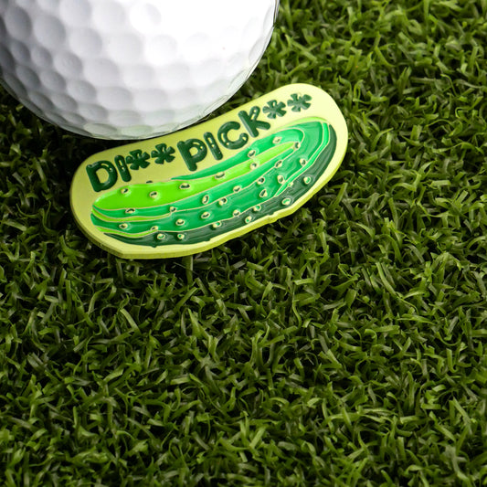 A golf ball sits on turf next to Logie Joe’s Golf Dill Pickle Ball Marker, a novelty marker shaped like a dill and labeled "DI PICK" in star letters—perfect for sparking locker room laughs.