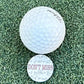 The Grunk Dolfer Don't Miss Ball Marker, featuring bold red text and surrounded by handwritten math formulas, sits on artificial grass beside a golf ball—making it a perfect unique golf gift.