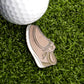 A close-up of a golf ball on artificial grass next to the Ballmarkers.com Yo Guy Slip-On Loafer Ball Marker, shaped like a comfortable shoe.