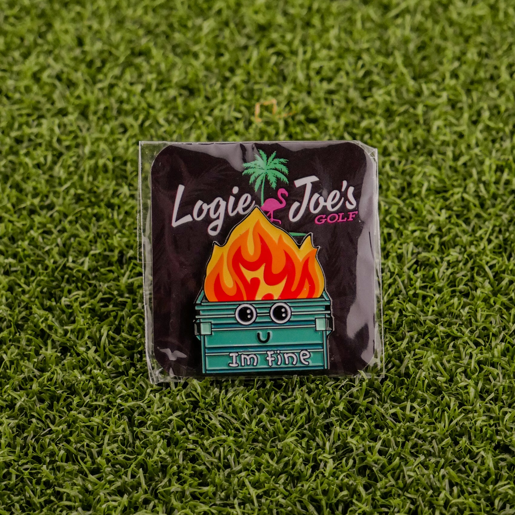 The Dumpster Fire pin by Ballmarkers from Logie Joes features a smiling cartoon dumpster with flames and Im fine. This humorous golf accessory doubles as a personalized ball marker, displayed on a Logie Joe’s Golf card atop green turf.