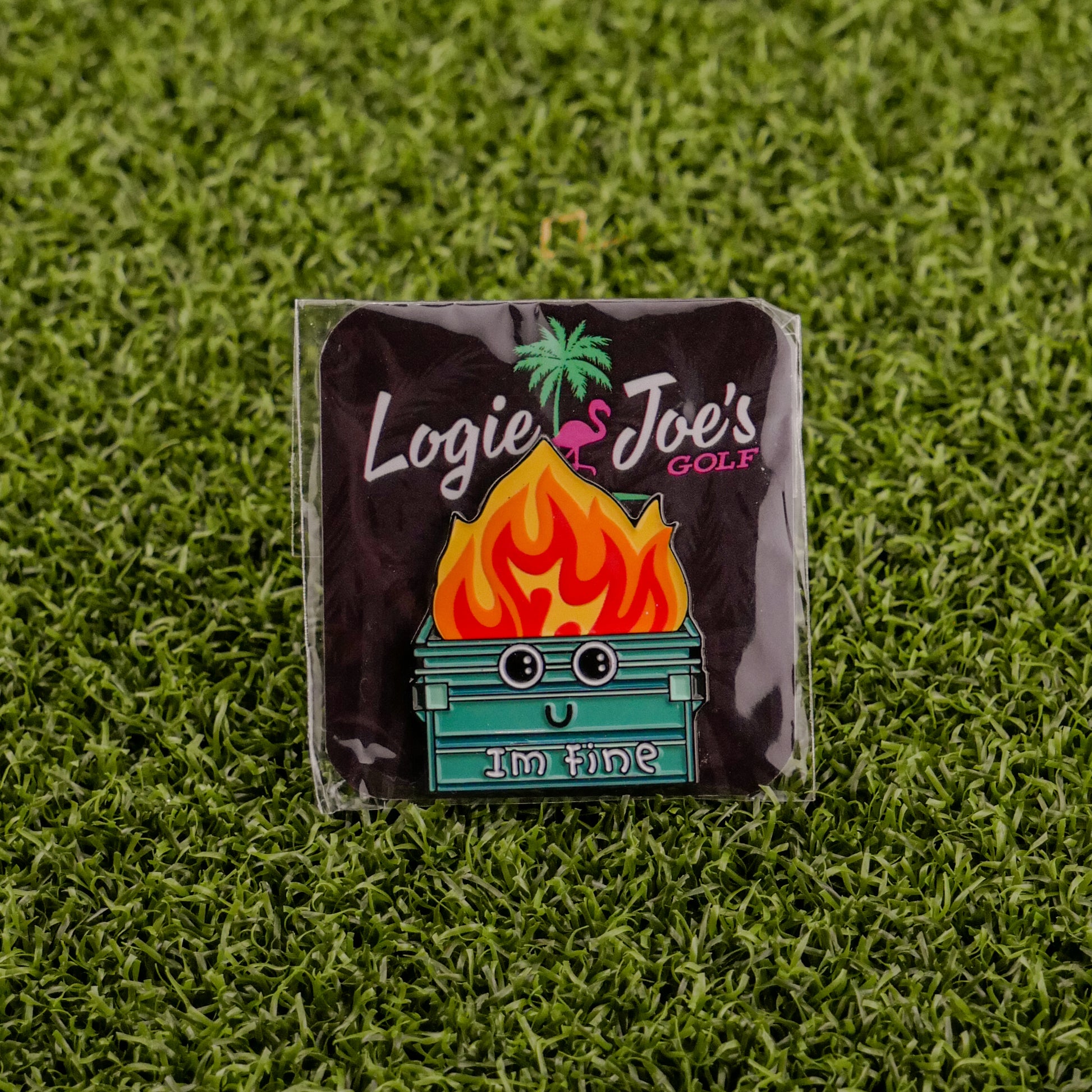 The Dumpster Fire pin by Ballmarkers from Logie Joes features a smiling cartoon dumpster with flames and Im fine. This humorous golf accessory doubles as a personalized ball marker, displayed on a Logie Joe’s Golf card atop green turf.
